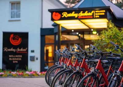 Eingang des Residenz Seehotel mit beleuchtetem Schild und einer Reihe roter Leihfahrräder, ideal für Gäste, die die Umgebung erkunden möchten, mit Fokus auf Wellness, Business und Spa.