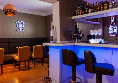 Stilvolle Hotelbar im Residenz Seehotel mit moderner blauer Beleuchtung, eleganten goldenen Barhockern und einer umfangreichen Auswahl an hochwertigen Spirituosen, perfekt für abendliche Entspannung und Geselligkeit.