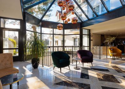 Helle und offene Lobby des Residenz Seehotel mit großzügigen Fensterfronten und einem einzigartigen Glasdach, das natürliches Licht hereinlässt, ausgestattet mit stilvollen, farbigen Sesseln und eleganten hängenden Lampen, ideal für einen entspannten Aufenthalt.